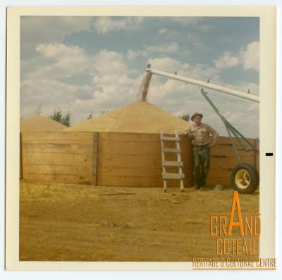 Photographic print, Joe Richtik standing in front of a grain bin while it is being filled
